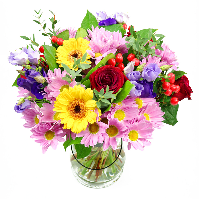 Set against a crisp white background, this expansive mixed bouquet rises confidently from a clear glass vase, its colours and textures reminiscent of an early morning walk through Covent Garden's flower stalls. At the centre, rich red roses open in velvety spirals, their deep, saturated hue providing a romantic anchor that immediately catches the eye. Just beside them, two golden yellow gerberas with dark brown-orange centres beam outward, giving the arrangement a bright, optimistic character. Encircling these focal blooms, soft pink daisies or chrysanthemums gather in generous clusters, each bloom boasting many fine petals and a tiny yellow centre, creating a cushion of gentle colour that softens the bouquet's overall look. Threaded through are elegant lisianthus blooms in shades of purple and lavender, some tightly budded and others fully open, their bell-shaped flowers adding sculptural interest and a cool, sophisticated contrast to the warmer tones. Scattered throughout the design, plump red hypericum berries lend a distinctive roundness and a glossy finish, like little bursts of festive detail. The flowers are enveloped by a rich variety of green foliage, from broad, darker leaves that frame the base to airy, light-green sprigs that reach outward, giving the piece movement and a natural, garden-inspired feel. The clear vase allows you to see the carefully arranged stems, all neatly cut to sit just so in clean water, reflecting the practiced hand of a skilled florist. This bouquet feels ideal for marking life's joyful moments in Covent Garden-perhaps a celebration dinner near Neal Street, a thank-you gesture for a theatre host, or simply to bring a living, colourful centrepiece into a bright city apartment.